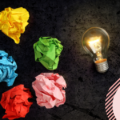 An image of a lit up light bulb and 5 colourful scrunched up pieces of paper - image depicting a lack of ideas.