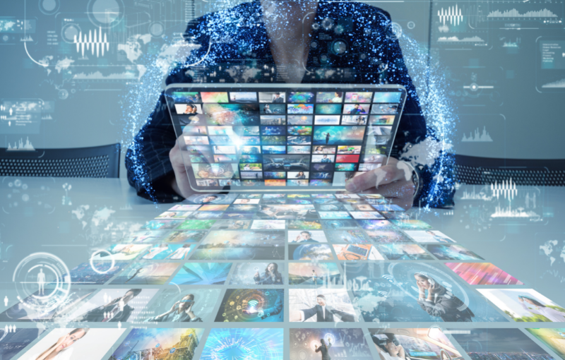 A person sitting at a desk, holding a tablet in their hands. The table features roughly 100 images in the form of small icons.